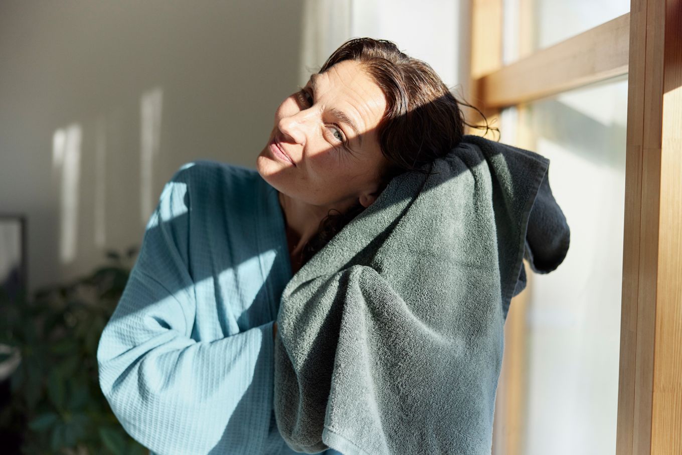 Kvinna står i morgonrock med blött hår och kramar det med en handduk.