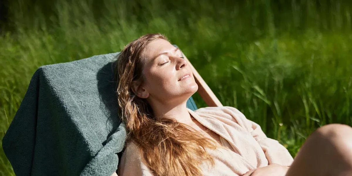 Kvinna ligger i en solstol och solar. Hon blundar och ler mot solen.