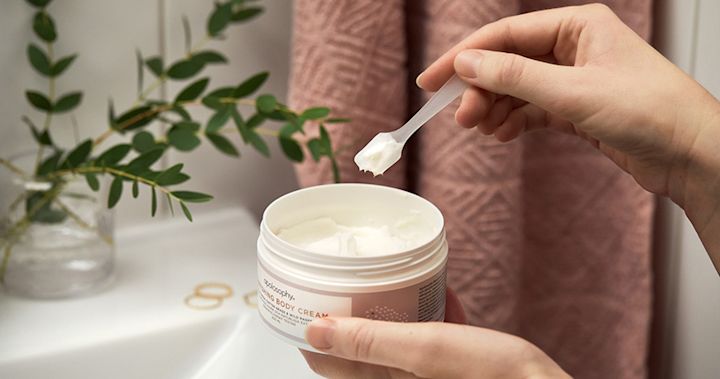 En person tar hudkräm med en liten spatel från en rund hudvårdsprodukt.