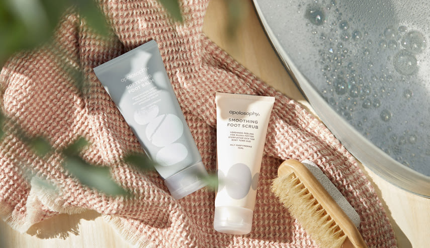 På en handduk ligger två produkter från Apolosophys fotvårdsserie, samt en borste.