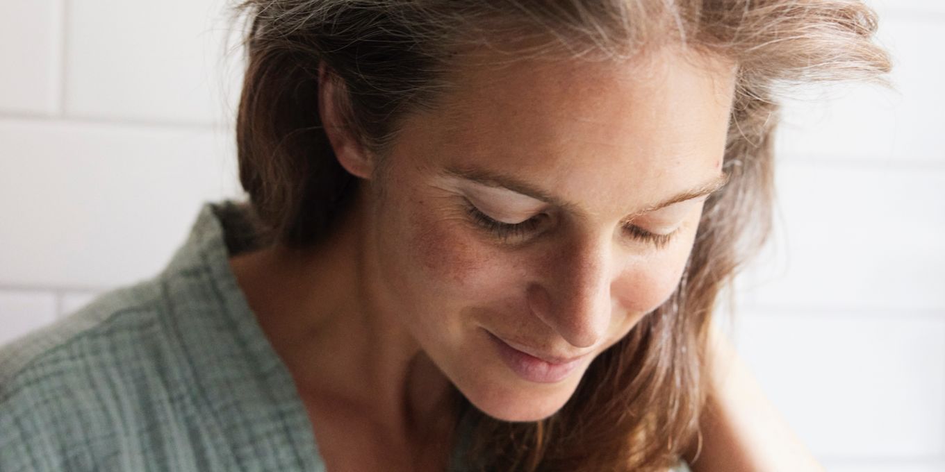 Kvinna står i ett badrum och rör vid sitt hår. Hon tittar ner.