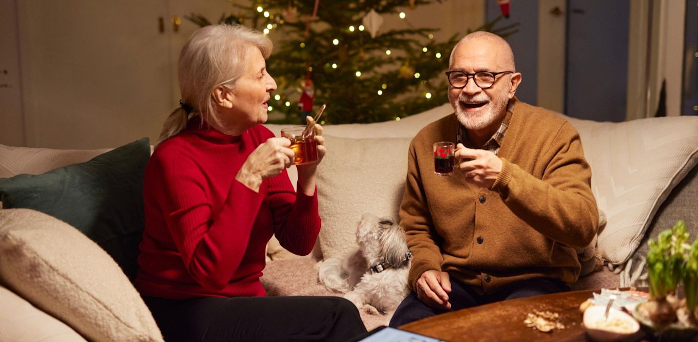 Ett äldre par sitter i soffan och dricker glögg under julen.