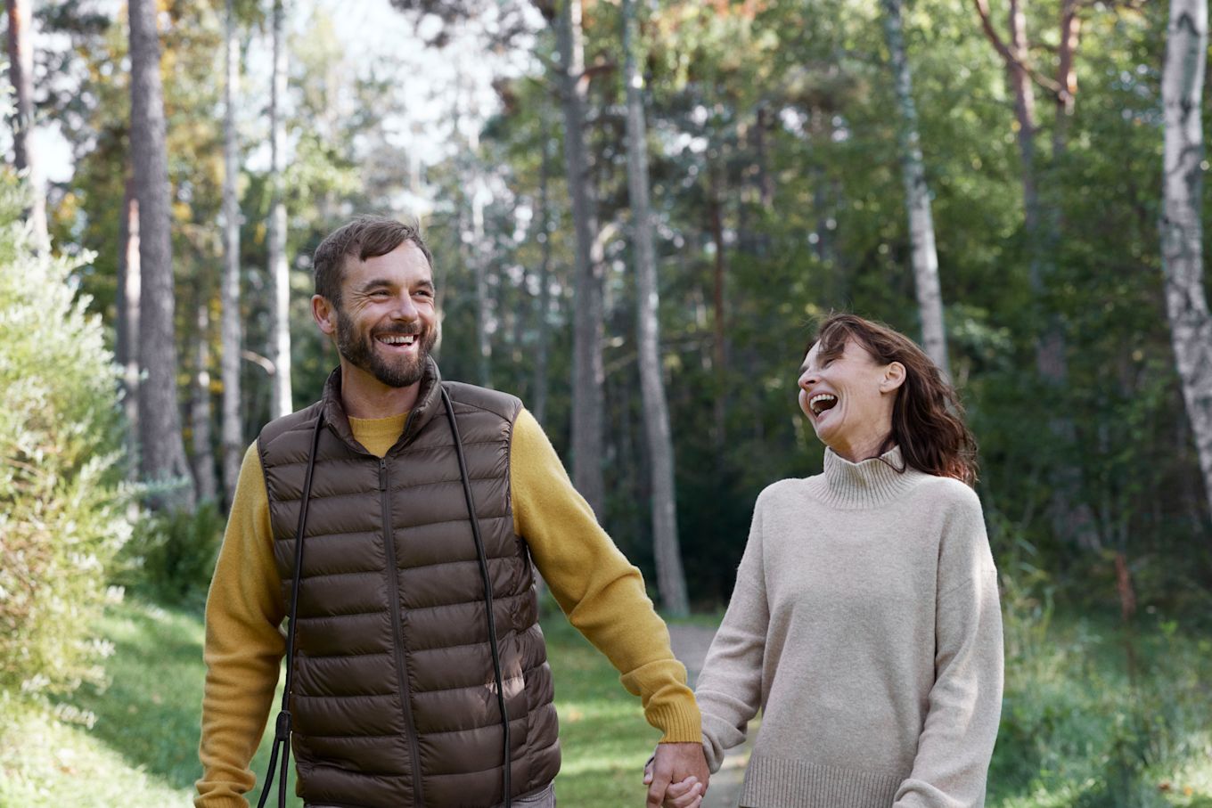 Man och kvinna promenerar ute i skogen, håller hand och skrattar tillsammans.