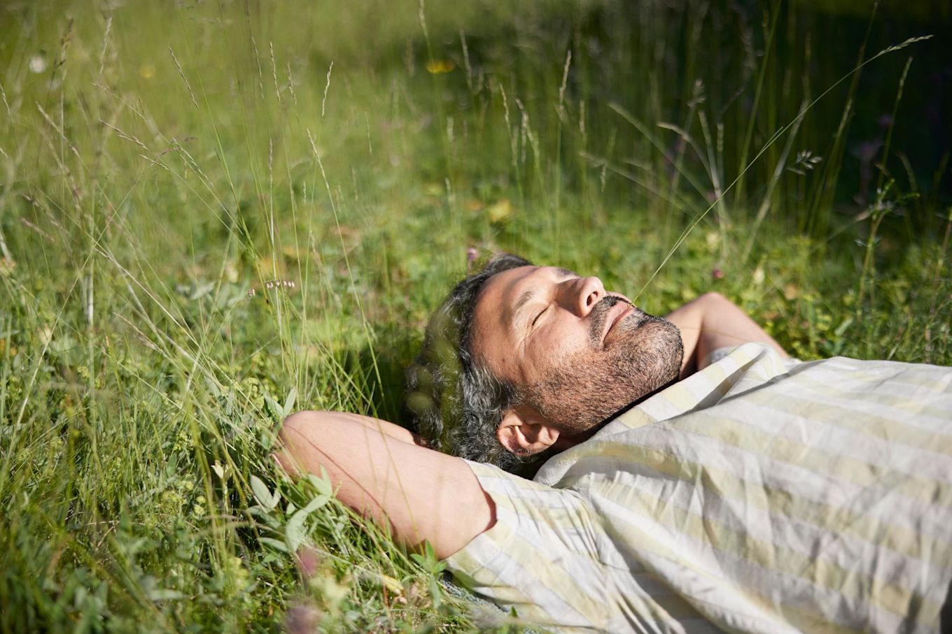 En man ligger ute på en gräsmatta på sommaren och blundar i solskenet.