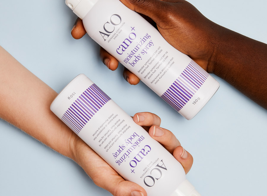 Två händer håller i varsin flaska med ACO Cano+ moisturizing body spray.