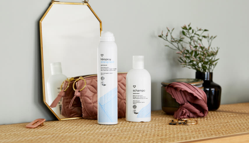 På en byrå står två produkter från Apotek Hjärtats hårvårdsserie, schampo och hårsspray.