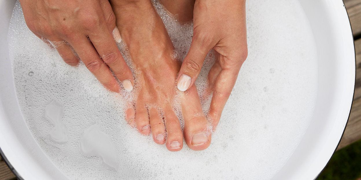 Fot och hand i ett fotbad med skum.