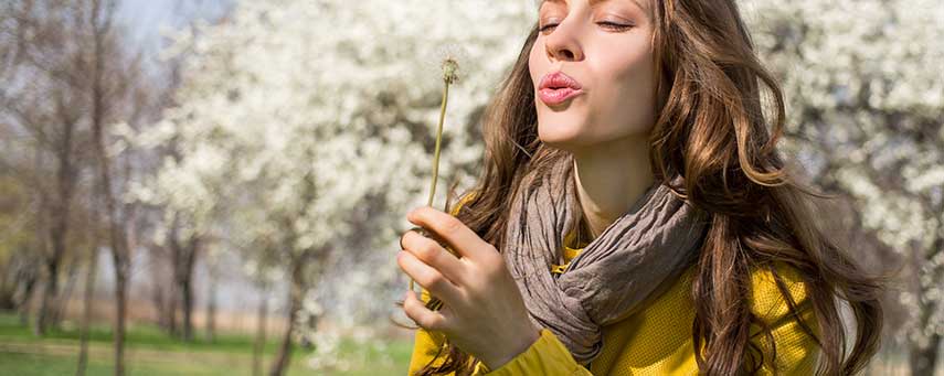 En kvinna står i vårsolen i en park och blåser på en