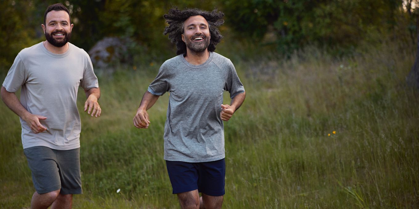 Två män är ute och springer barfota i gräset på sommaren, iklädda shorts och t-shirt.