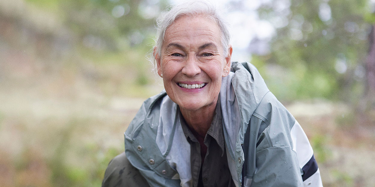 Kvinna är i skogen och ler mot kameran.