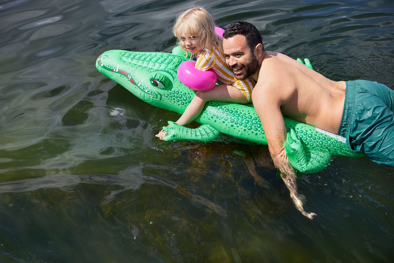 Pappa och dotter är ute på sommaren och leker i vattnet på en uppblåsbar krokodil.