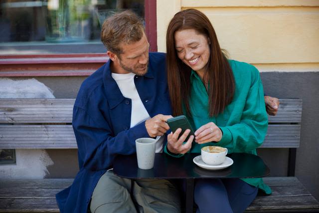 En man och en kvinna håller om varandra på en uteservering och tittar i en mobil.