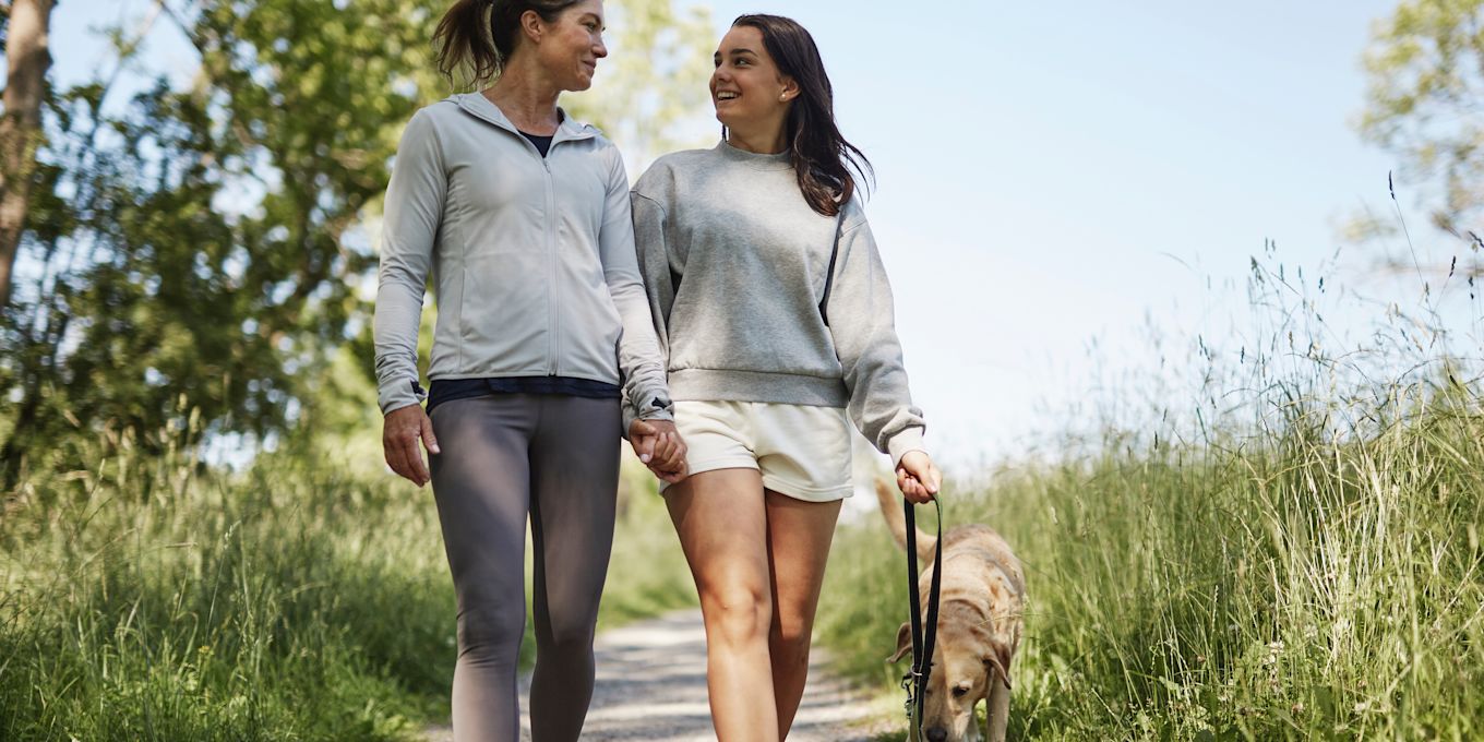 Tonårsdotter och mamma är ute och går på en promenad utomhus och pratar glatt med varandra.