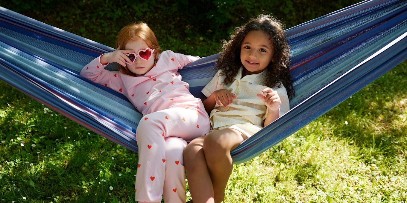 Två flickor sitter i en hängmatta och tittar in i kameran. Den ena flickan har hjärtformade solglasögonen på sig.