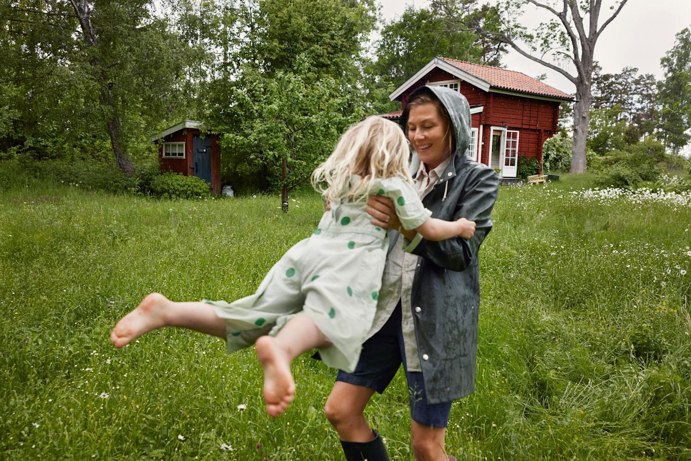 Mamma och dotter leker ute i gräset på sommaren, mamma lyfter upp dottern och svänger runt med henne.