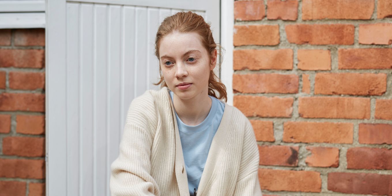 Tonårstjej sitter utanför ytterdörren och tittar åt sidan.